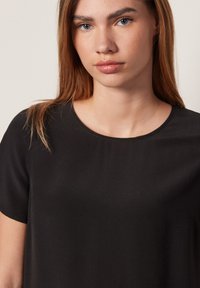 Svart kortärmad topp med rund halsringning, tillverkad av ett slätt tyg. Har en avslappnad passform och minimala sömnadsdetaljer.