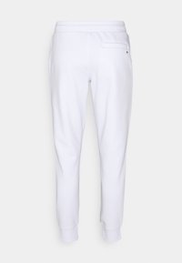 White sweatpants with a soft texture, tapered legs, and an elastic waistband. Features a single back pocket and minimal branding accent.