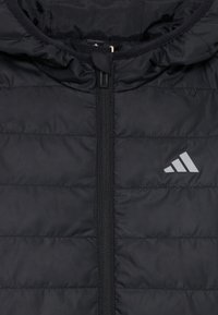 Veste isolée noire avec capuche, design matelassé vertical, fermeture éclair sur toute la longueur et logo Adidas en gris sur la zone de la poitrine gauche.