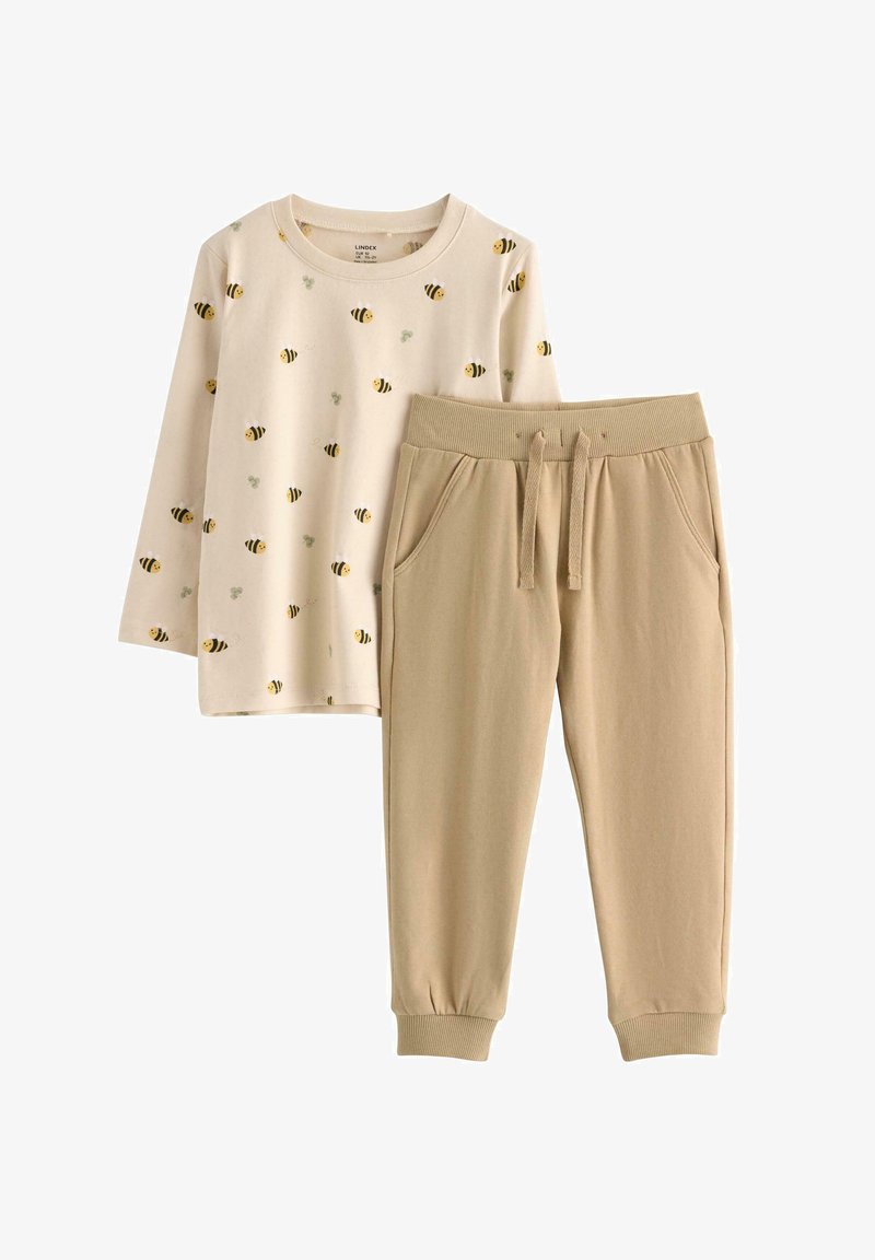 Dwuczęściowy strój składający się z kremowej koszuli z długim rękawem z nadrukiem pszczół oraz beżowych bawełnianych spodni dresowych z elastycznym pasem i mankietami.