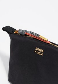 Czarna torba z tkaniny z złotym suwakiem, z teksturowanym uchwytem do suwaka oraz wytłoczonym logo marki z boku. Prosty i funkcjonalny design.