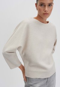 Maglione beige chiaro in morbido tessuto, con scollo ampio, maniche a tre quarti e vestibilità comoda. Cuciture evidenti all'orlo e ai polsini.