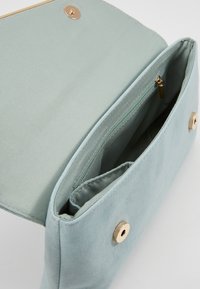 Světle modrá kabelka vyrobená z měkké tkaniny, s uzávěrem na zlatý cvok a vnitřní kapsou na zip. Hladká textura, minimalistický design.