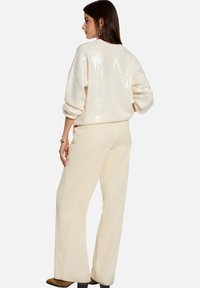 Pull blanc à sequins avec manches larges retroussées, assorti à un pantalon en velours côtelé beige clair, doté d'un tissu texturé et d'une coupe large.