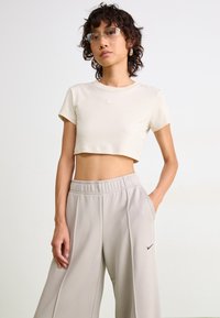 T-shirt cropped beige clair à manches courtes avec un petit logo sur la poitrine, associé à un pantalon ample gris clair avec des poches.