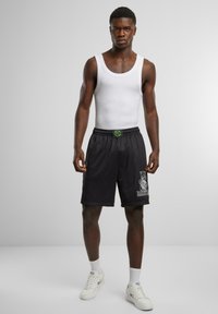 Pantaloni da basket in rete nera con cintura regolabile e stampa del logo. Abbinati a una canotta bianca semplice e scarpe da ginnastica bianche.