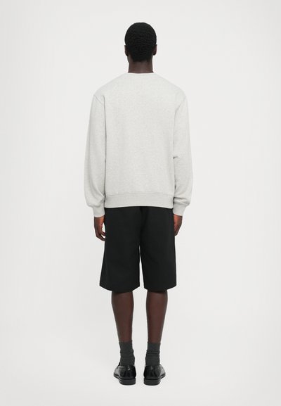 Lys grå genser med ribbestrikkede mansjetter og hem, kombinert med svarte shorts. Enkel design med avslappet passform, sett fra baksiden.