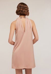 Rochie fără mâneci, de culoare roz pal, cu guler tip halter și spate adânc în V. Construită dintr-un material neted, prezintă pliseuri și accente metalice la decolteu.