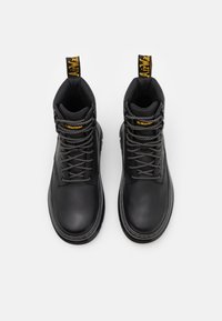 Bottes chevilles en cuir noir avec lacets gris et une languette jaune, présentant une texture lisse et un design à bout arrondi.