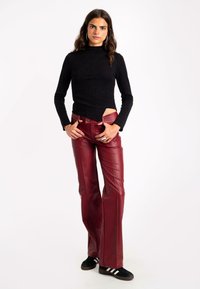 Top negro ajustado de manga larga combinado con pantalones de cuero de campana en rojo oscuro. La modelo se presenta con confianza, vistiendo zapatos negros con rayas blancas.