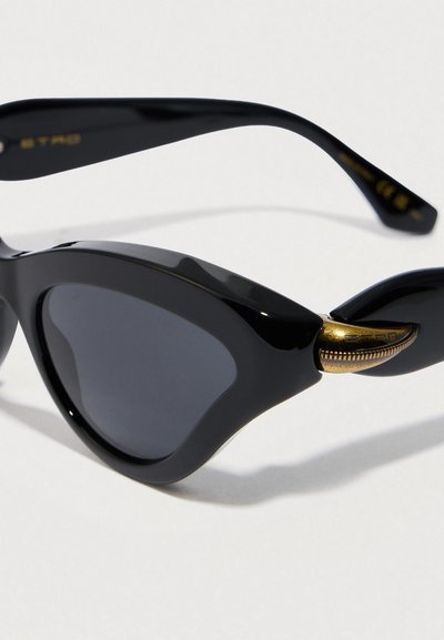 Occhiali da sole a occhi di gatto in plastica nera con lenti scure e dettagli accentati in tono oro sulle stanghette. Texture liscia con finitura lucida.