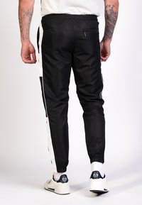 Schwarze, schmal geschnittene Jogginghosen mit weißen Seitenpanelen, elastischem Bund und Reißverschlusstasche, aus glattem, leichtem Material.