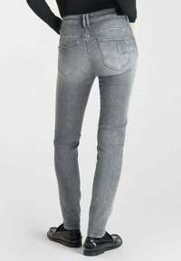 Un jean skinny gris avec une taille mi-haute, un minimum de décoloration, et deux poches arrière, associé à des mocassins noirs brillants.