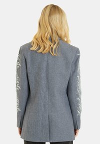 Blazer grigio con motivi floreali ricamati sulle maniche, design strutturato, testo liscio e vestibilità su misura. Vista posteriore mostrata.