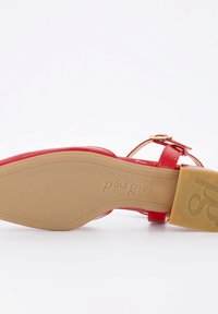 Sandalia de charol roja con una correa delgada en el tobillo y detalle de hebilla dorada. Presenta una suela beige con el grabado "paul green".