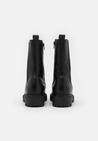 Botas de cuero negro hasta el tobillo con cremalleras laterales, superficie texturizada y suelas de goma gruesas. Parte trasera recta con tiradores para facilitar su colocación.