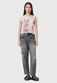 Kortærmet pink top med blomstermotiv, parret med slidte sorte jeans og sorte sandaler. Sættet har en afslappet pasform og synlige huller.