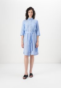 Light blue button-up dress with three-quarter sleeves, a tie belt at the waist, and a textured fabric. Worn with black open-toe shoes.