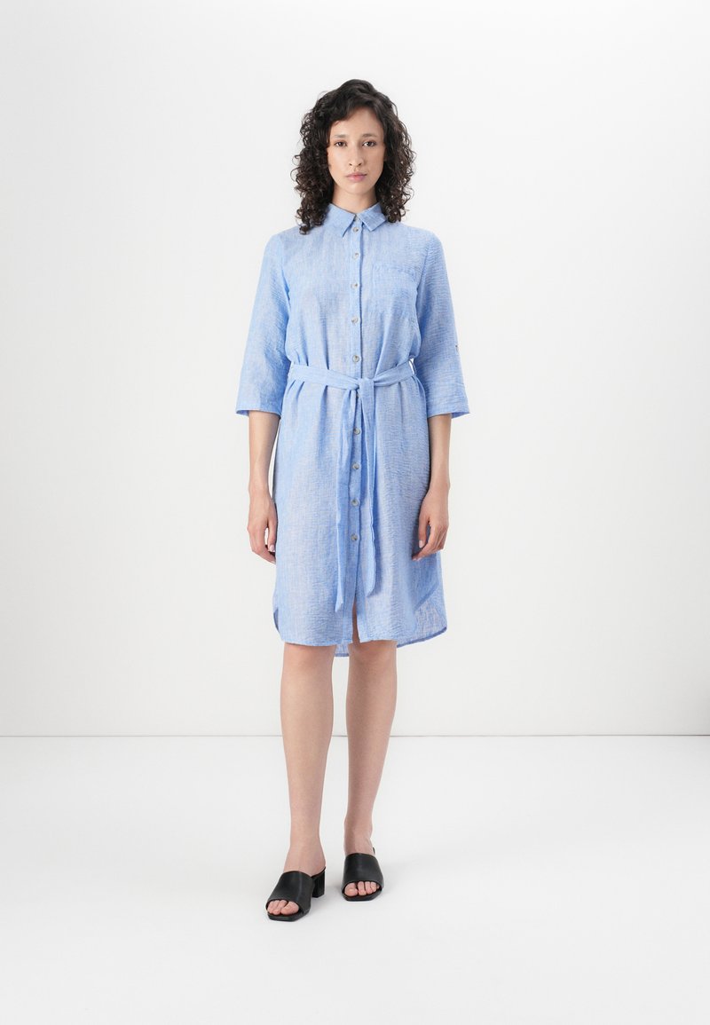 Light blue button-up dress with three-quarter sleeves, a tie belt at the waist, and a textured fabric. Worn with black open-toe shoes.
