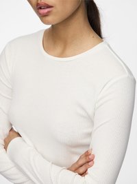 Top a maniche lunghe, a coste, di colore bianco sporco, con scollatura rotonda e design aderente. Il tessuto sembra morbido con una texture delicata.