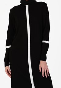 Robe noire en tricot avec des manches longues, un col montant et une bande blanche centrale sur le devant avec des accents blancs sur les manches.