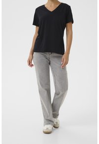 Svart kortärmad V-ringad topp tillsammans med ljusgrå raka jeans. Modellen bär vita och beige sneakers. Enkel, avslappnad design.