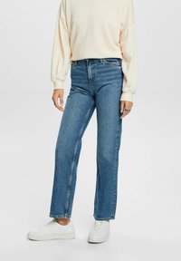 Jeans de mezclilla azul claro con corte recto, cintura alta y costuras mínimas. Combinados con un suéter crema y zapatillas blancas.