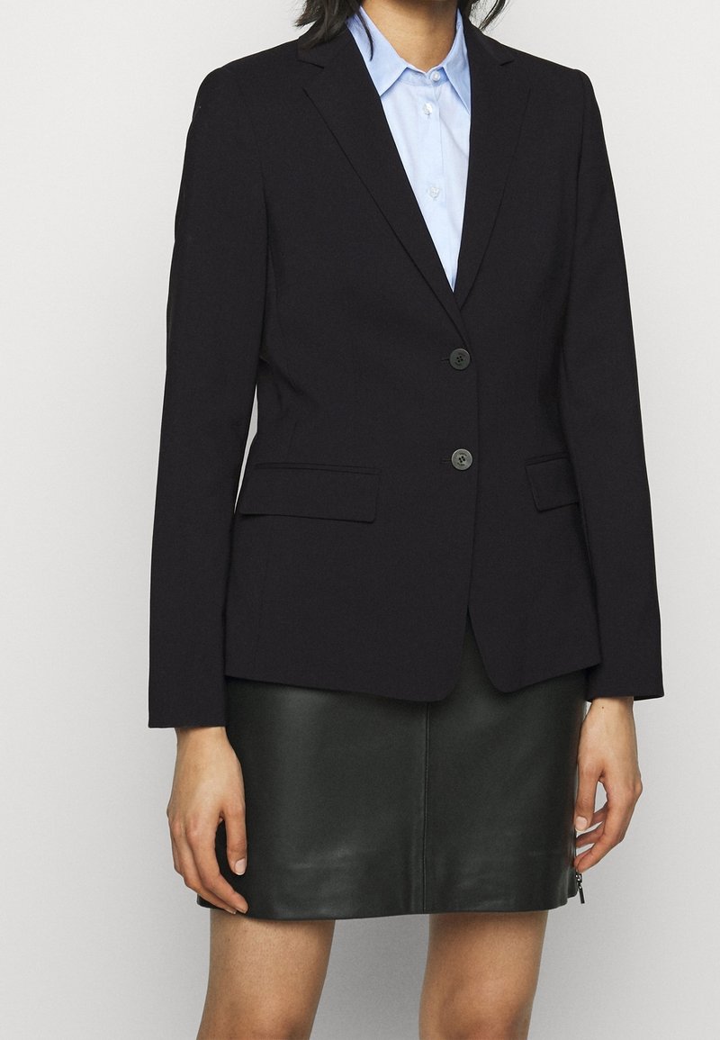 Svart skräddarsydd blazer med två knappar, slagkrage och sidofickor, parat med en ljusblå skjorta med krage och lädjerock.