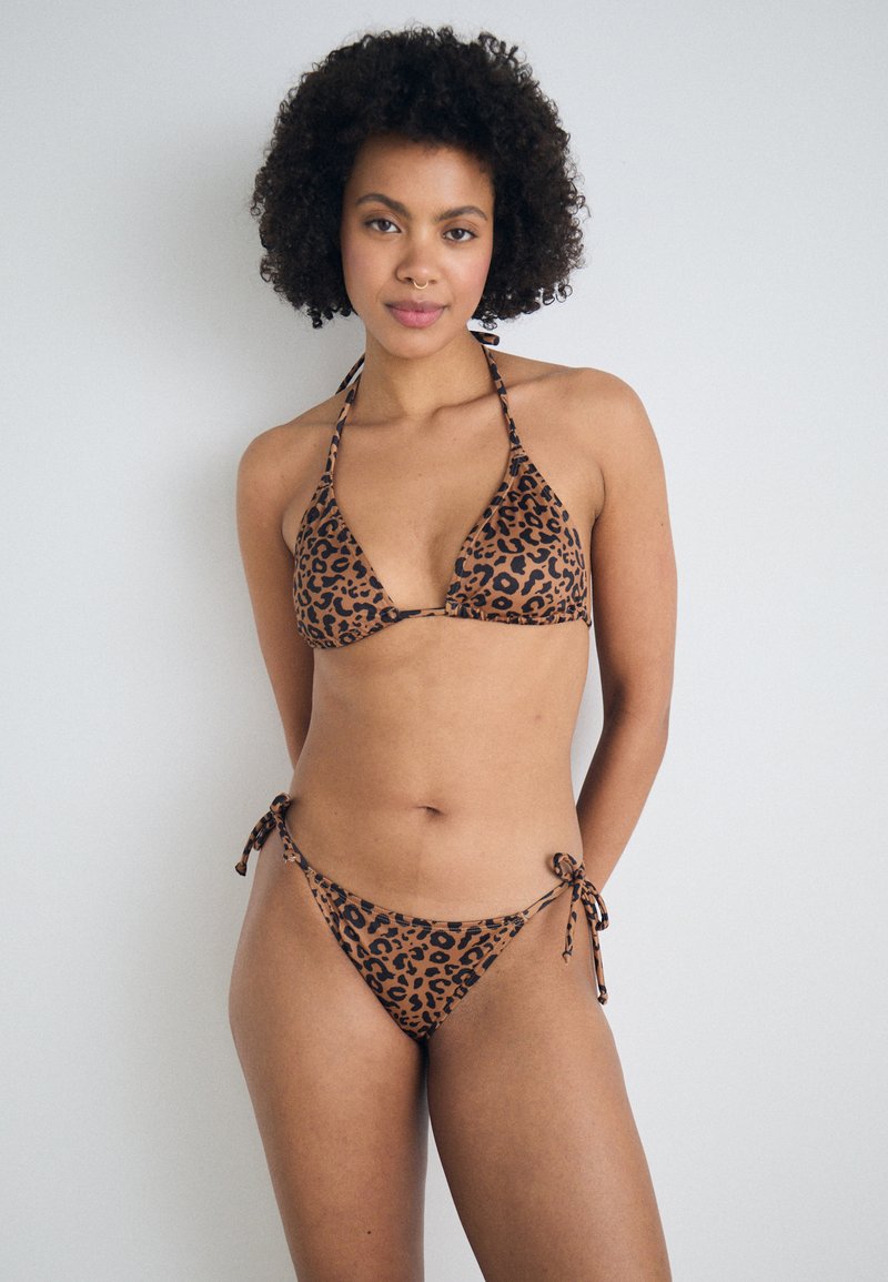 Bikini set s uzorkom leoparda, s trokutastim topom na vezanje oko vrata i donjim dijelom s podesivim vezicama sa strane. Boje su smeđa i crna.