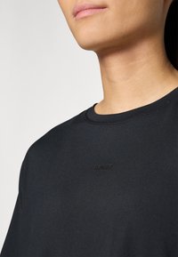 Black athletic t-shirt with a smooth texture and crew neckline, featuring a subtle embossed "STRONGER" logo on the front.