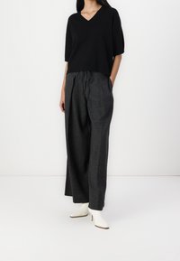 Suéter negro de manga corta y cuello en V combinado con pantalones grises de pierna ancha. Los pantalones tienen un cinturón elástico en la cintura y bolsillos laterales. Botas blancas hasta el tobillo.