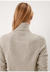 Pull gris clair en maille avec un col montant, présentant un petit détail bouton dans le dos. Texture douce avec des manches longues.