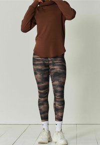 Bruin langemouwen top met een kraag, gecombineerd met zwart en bruin tie-dye legging, en chunky witte sportschoenen met accenten.