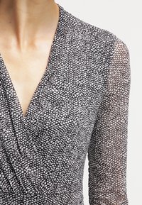 Omwrap klänning med ett svart och vitt strukturerat mönster, med långa ärmar och V-ringning, tillverkad av ett lätt, genomskinligt tyg.