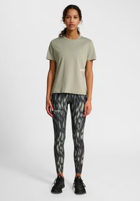 Ljusgrön t-shirt med kort ärm och svarta leggings med ett grönt abstrakt mönster, kombinerat med svarta träningsskor. "Hummel"-logotyp synlig.