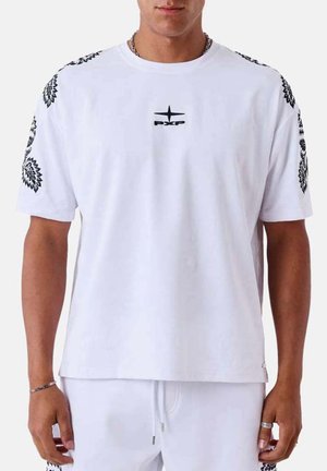 Homme portant une chemise blanche à manches courtes avec des motifs floraux noirs sur les manches et un petit logo PXP noir sur la poitrine.