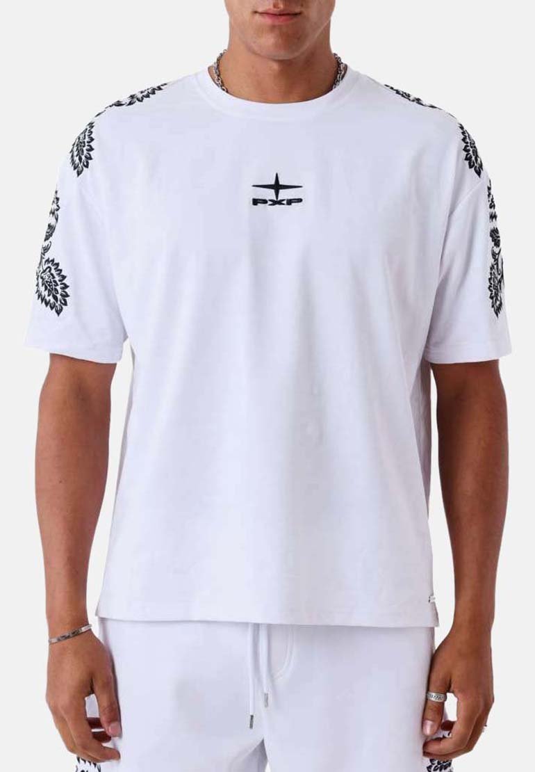 Homme portant une chemise blanche à manches courtes avec des motifs floraux noirs sur les manches et un petit logo PXP noir sur la poitrine.