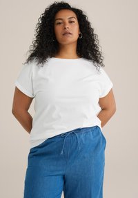 Camiseta blanca de manga corta con puños enrollados, combinada con pantalones azul con cordón, ambos confeccionados en una tela suave y transpirable.