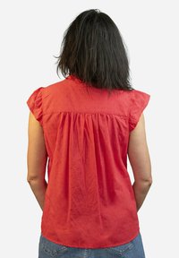 Blusa roja de manga corta con volantes en las mangas, con la parte trasera fruncida y un patrón texturizado. Material de algodón, corte relajado y dobladillo curvo.