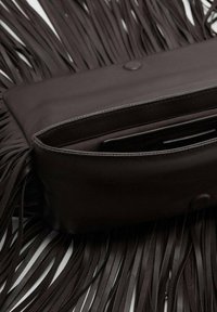 Pochette en cuir marron avec des détails à franges, présentant un extérieur lisse, une fermeture magnétique et une poche intérieure pour l'organisation.