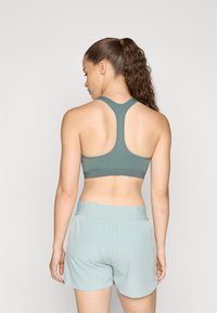 Sostén deportivo verde con diseño de espalda nadadora, combinado con pantalones cortos verde claro. Textura suave con bandas elásticas en la cintura.