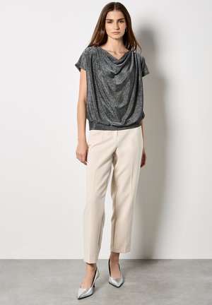Top corto gris brillante de manga corta con escote drapeado, combinado con pantalones cremosos a medida y tacones plateados de punta.