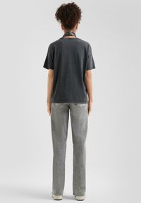 Grijze t-shirt met korte mouwen in een relaxte pasvorm, gecombineerd met lichtgrijze rechtlopende jeans. Een bandana om de hals geknoopt. Eenvoudig ontwerp, minimale details.