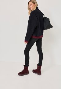 Pulover negru din polar cu accente marsala, asortat cu blugi negri skinny și cizme burgundy cu șiret, însoțit de o geantă neagră.