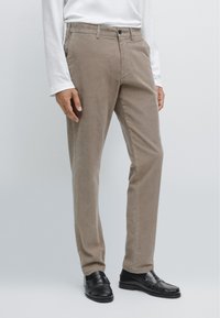Pantaloni in velluto a coste beige con vestibilità dritta. Presentano una chiusura a bottone, passanti per cintura e tasche laterali. Abbinare mocassini neri aggiunge contrasto.