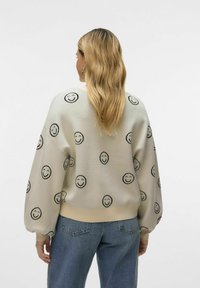 Jasnobeżowy sweatshirt z czarnym wzorem uśmiechniętej buźki, z balonowymi rękawami i prążkowanym dołem. W połączeniu ze średnio spranymi dżinsami.