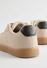 Beige ruskind sneakers med en sort læderhæl, tekstureret gummisål og kontrasterende syninger.