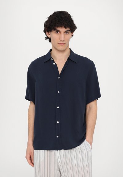 Chemise courte à manches courtes de couleur marine avec un col, présentant un devant boutonné et un tissu léger. Texture lisse et coupe décontractée. Pantalon à rayures verticales.