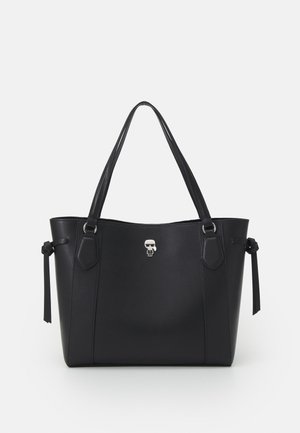 Sac fourre-tout en cuir noir avec deux bretelles d'épaule, des détails noués sur les côtés, et un petit emblème argenté en forme de caractère au centre avant.