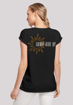 Schwarzes T-Shirt mit kurzen, umgeschlagenen Ärmeln, das eine Sonnengrafik und den Text "HALT DEINE SONNENSEITE NACH OBEN" in Weiß und Orange zeigt.